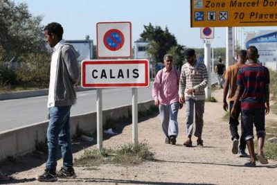 Migrants pass by a road sign as they leave the northern area of the camp called the "Jungle" in Calais